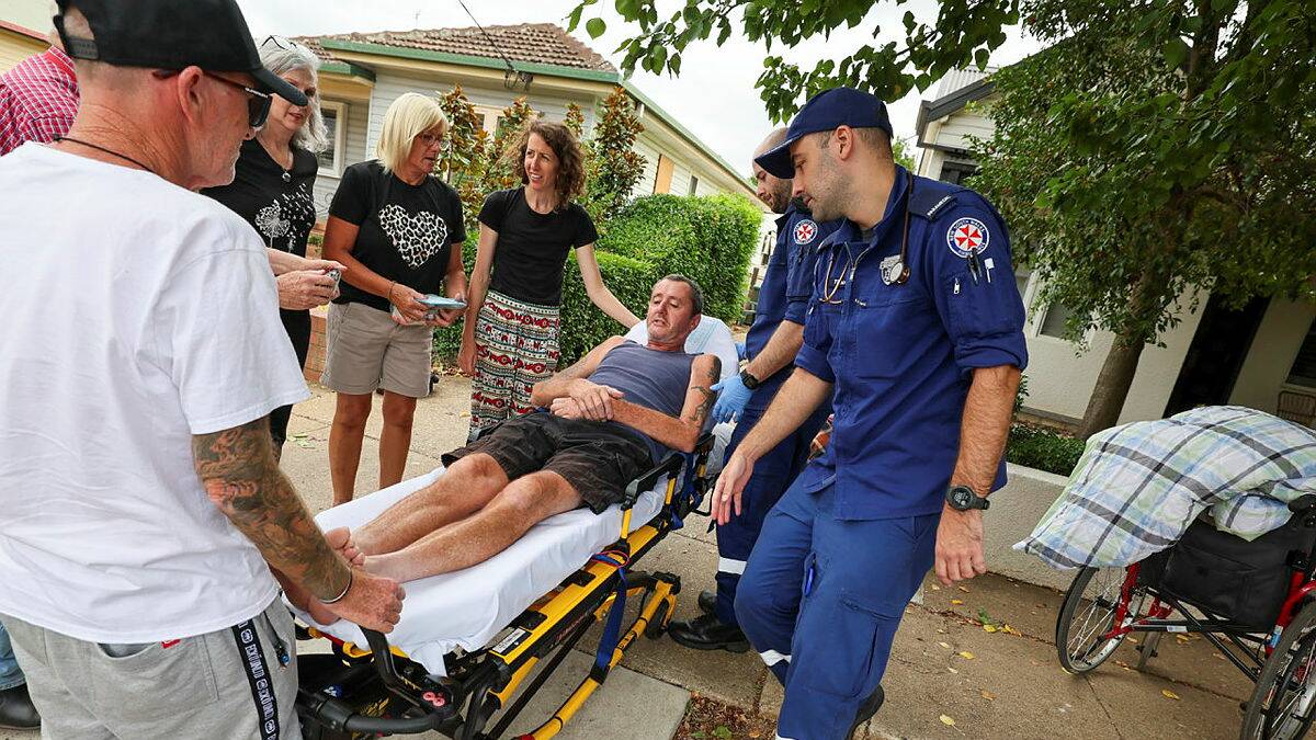 Warren Acott with family and friends as paramedics take him to hospital after he fell from a wheelchair in Central Wagga on Sunday morning. Picture by Les Smith