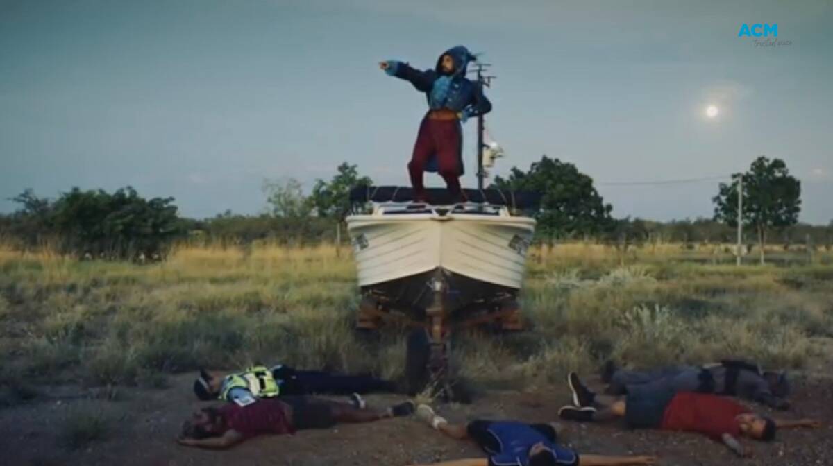 A still from 'This is Australia' showing a figure dressed as Captain Cook standing on the bow of a boat in a field. Picture by Marrugeku. 