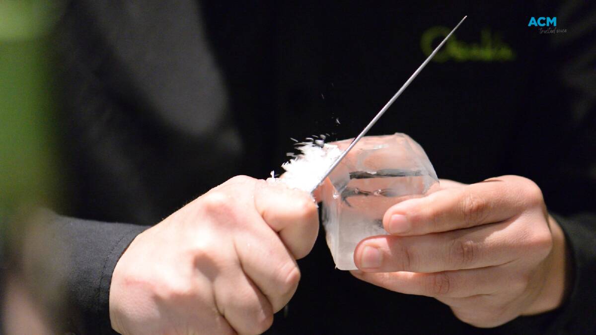 A bartender shaves the edges from a block of ice using a knife. File picture.