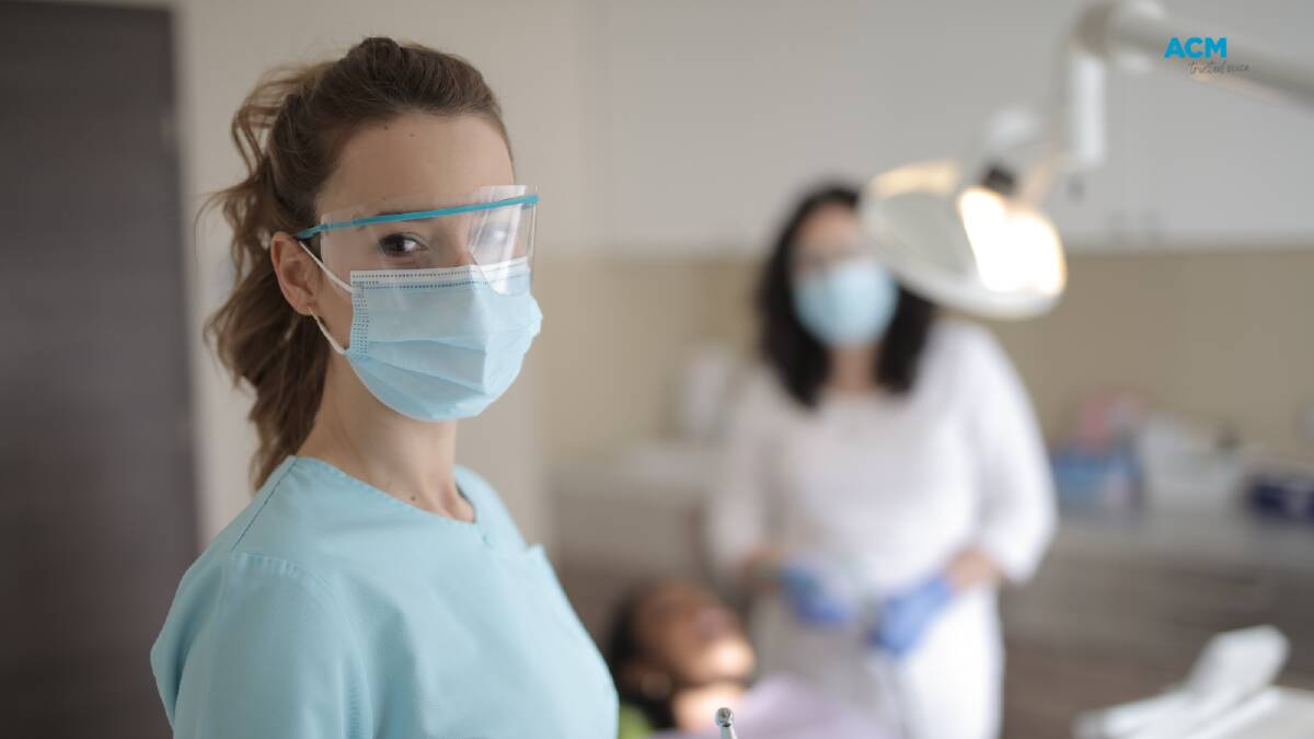 A young dental care worker wears PPE in a clinic, with another worker and patient in the background. File picture. 