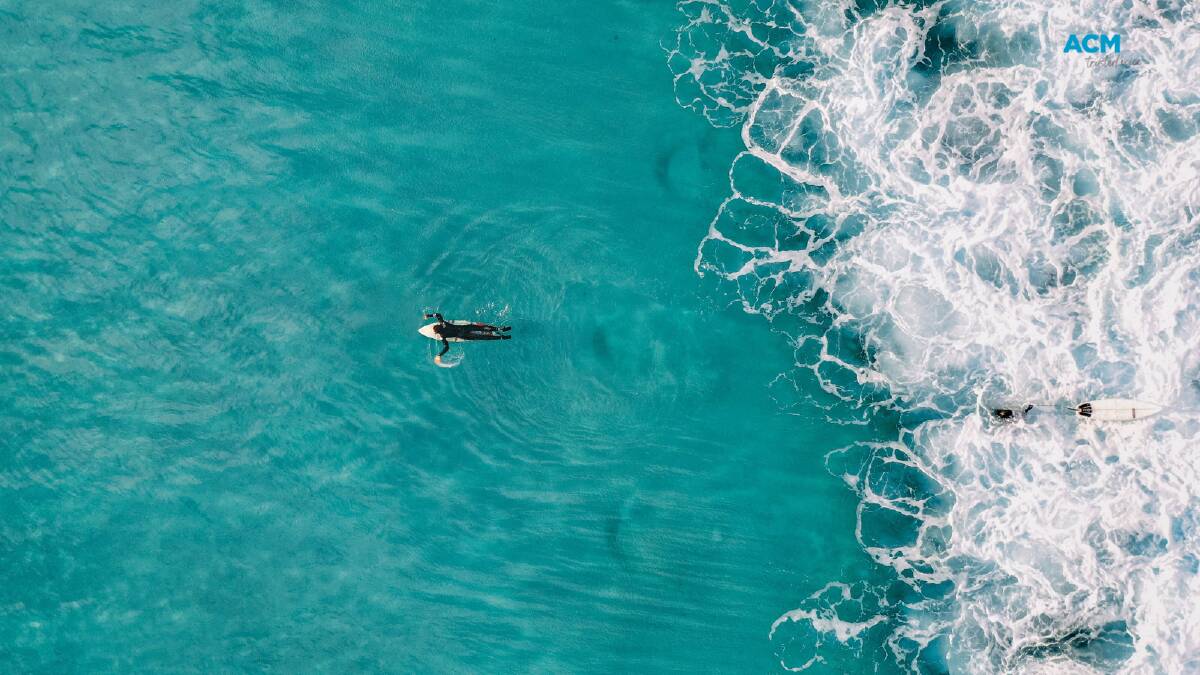 A surfer paddling in front of a wave. Picture by Kiril Dobrev via Canva