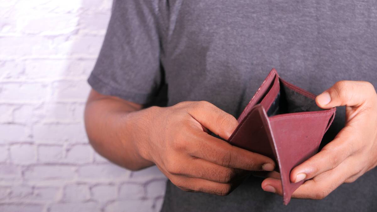 A man opens his empty wallet. Picture via Canva