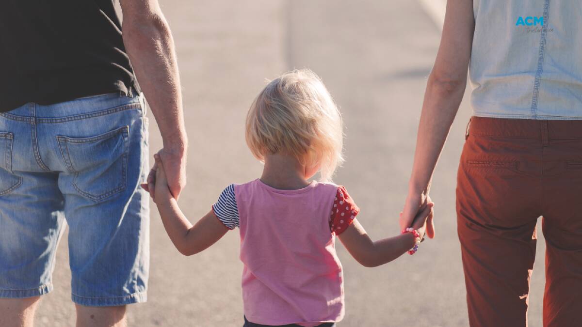 Parents hold their young child's hand. Picture via Canva