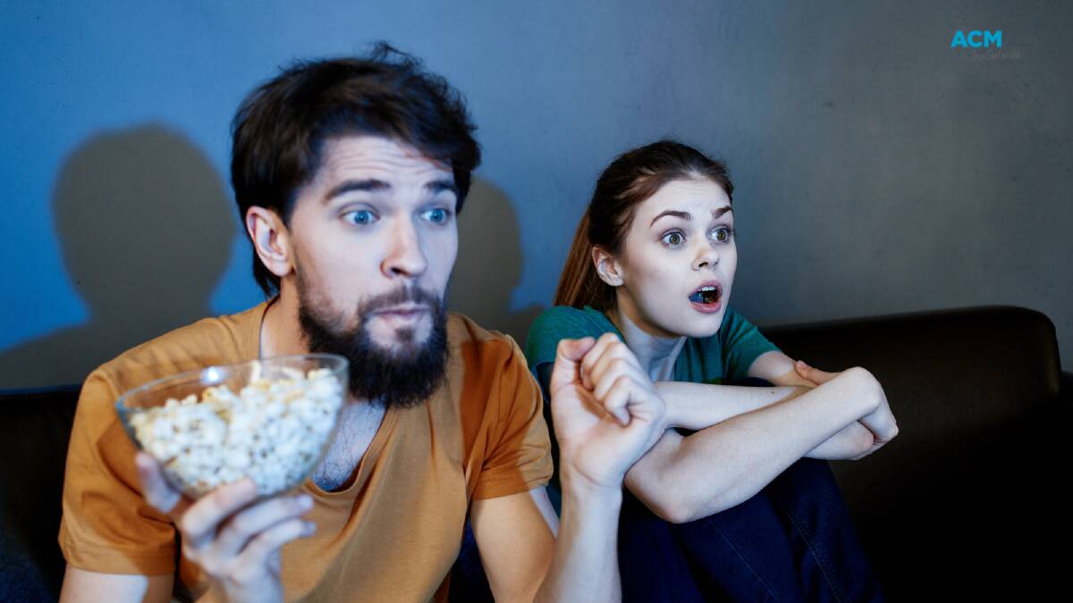 Two excited TV watchers stare at the screen. Picture via Canva