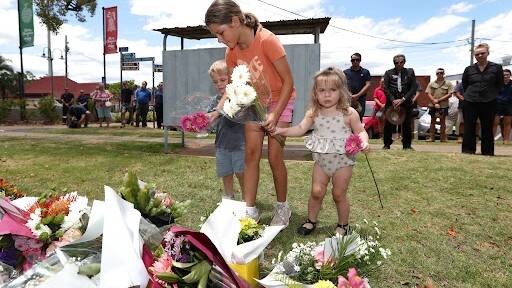 Children lay flowers in memory of the fallen officers at Chinchilla Police station in Queensland, Tuesday, December 13, 2022. Police have shot dead three people at a remote property on Queensland's Darling Downs after an ambush in which two officers and a bystander were killed. (AAP Image/Jason O'Brien)